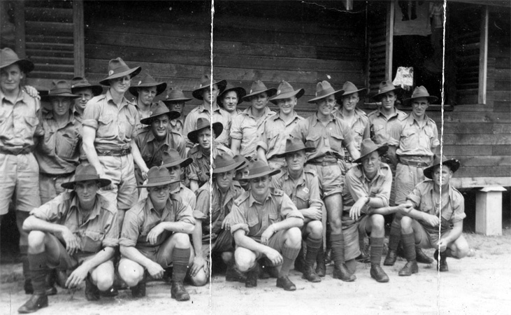 B Company, 12 Platoon
"No 12 Platoon taken outside our hut. Our Platoon Commander Lieut Head in front of my right shoulder."

Photo of "B" Company, 12 Platoon taken outside hut at Batu Pahat, Malaya.

Left to right (not confirmed):

Front row:
1) NX19760 - AUSTIN, Alfred Trevor (Crow or Alf), Pte. - B Company, 12 Platoon (right arm resting on knee)
2)  (left arm resting on knee)
3) (partly obscured)
4) NX32129 - HODGES, Alfred Edward (Fred or Snowy), Pte. - B Company, 12 Platoon (right hand on knee)
5) (partly obscrured between Alf HODGES and Harry HEAD)
6) NX70439 - HEAD, Harry, Lt. - B Company, O/C 12 Platoon (Officer with moustache)
7) NX26705 - WILSON, Harold Creswick (Cressy or Harry), Pte. - B Company, 12 Platoon
8) NX26599 - WATERSON, Stanley (Stan), Pte. - B Company, 12 Platoon (arms crossed over left knee)
9) NX29116 - BROWN, Raymond John Tresillian (Ray), Pte. - B Company, 12 Platoon (right arm resting on knee)

Back row:
1) NX26331 - HOLLAND, Bruce Hedley (Dutchy), Pte. - B Company, 12 Platoon
2) (hand on Dutchy HOLLAND's left shoulder)
3) (partly obscured in between ? and Allen GILBERT)
4) NX59100 - GILBERT, Allen John, L/Cpl. - B Company, 12 Platoon 
5) (standing at back with grimace on face)
6) NX27452 - SMITH, William Thomas (Bill), Pte. - B Company, 12 Platoon (leaning forward next to Allen GILBERT)
7) (standing at back with straight hat over eyes)
8) (crouching down next to Bill SMITH)
9) (standing with crease of photo running through his face)
10) (standing at back with hat pushed back)
11) 
12) (standing in between Harry WILSON and Stan WATERSON)
13) NX33051 - DEATH, William Frederick (Bill), A/Cpl. - B Company, 12 Platoon (standing with shirt undone)
14)
15) (standing with hands behind back)
Keywords: 080520a