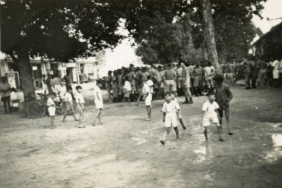 Malayan village
Malayan village.  Annotated on reverse:

"This snap is interesting because it shows the Aussie soldiers as the Australian public likes to imagine them - palying "two-up" in the street of a native village. Wherever you go you'll find one of these "rings", especially on pay-days. Note the children & locals who regard such events as everyday affairs & no longer take any notice of them"
Keywords: 20120722 NX30114